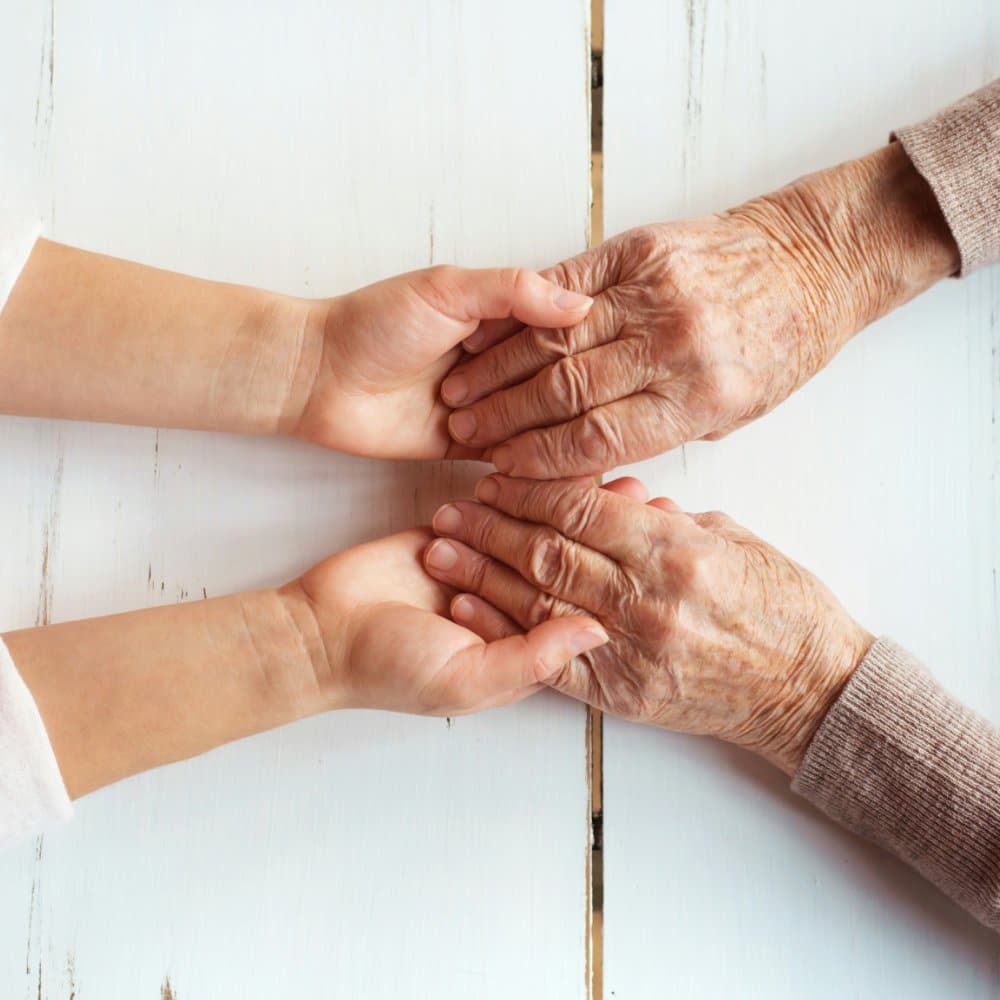 Two hands of different generations, going through Palliative care at home.