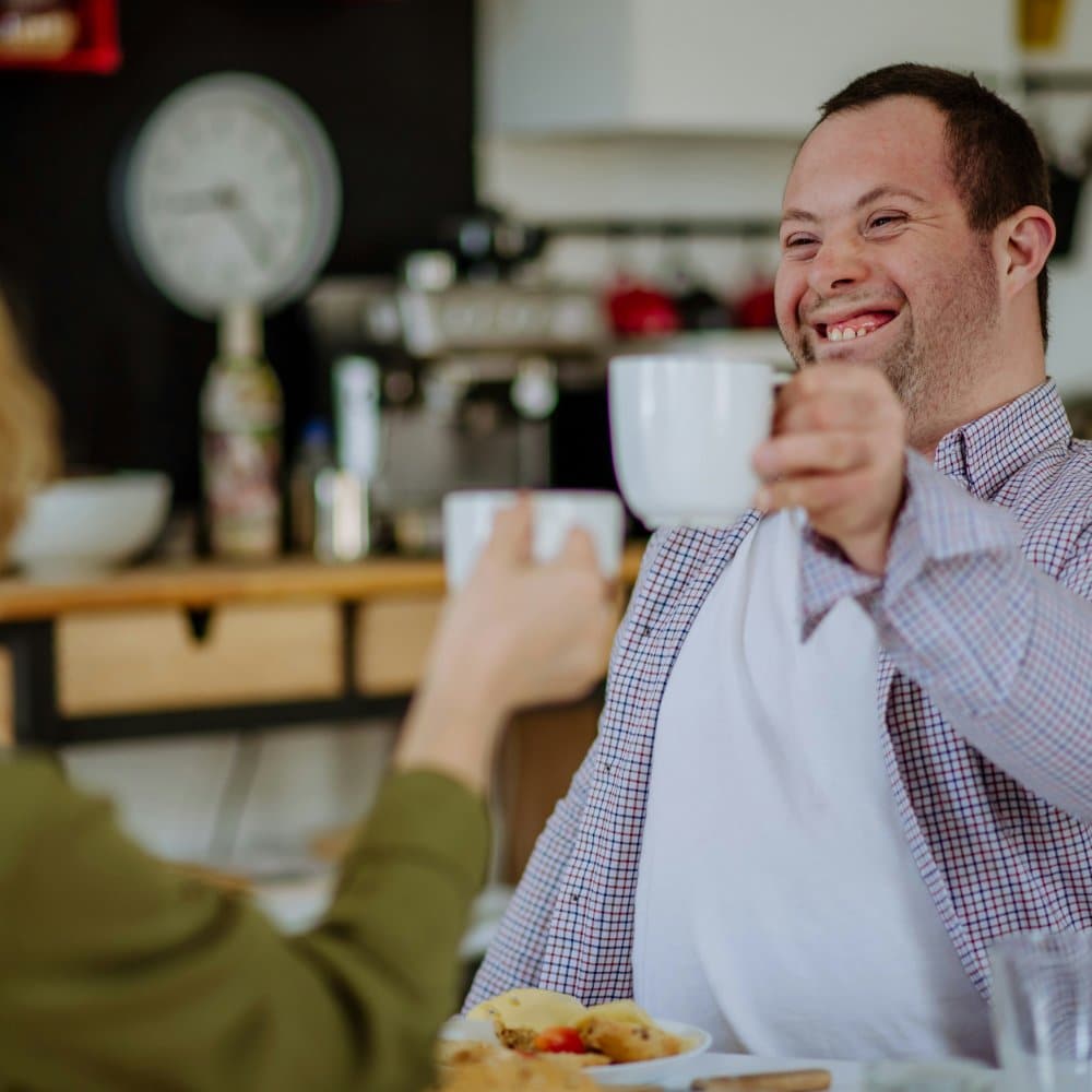 Two people sharing a meal together, a carer and a client. Client receiving adult learning disability care.